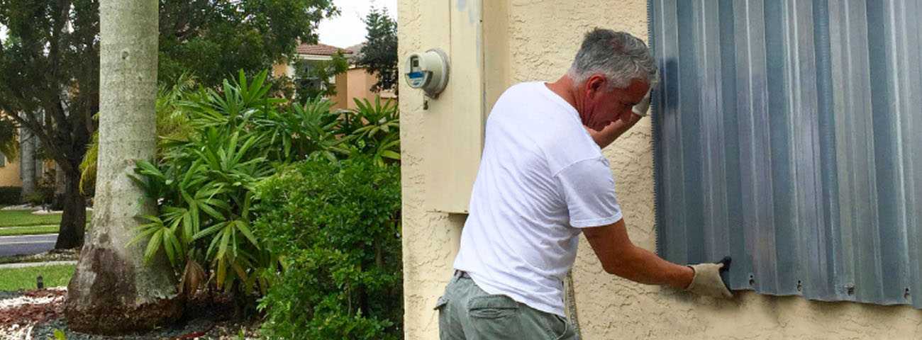 Gloved man installing sheet metal window shutters